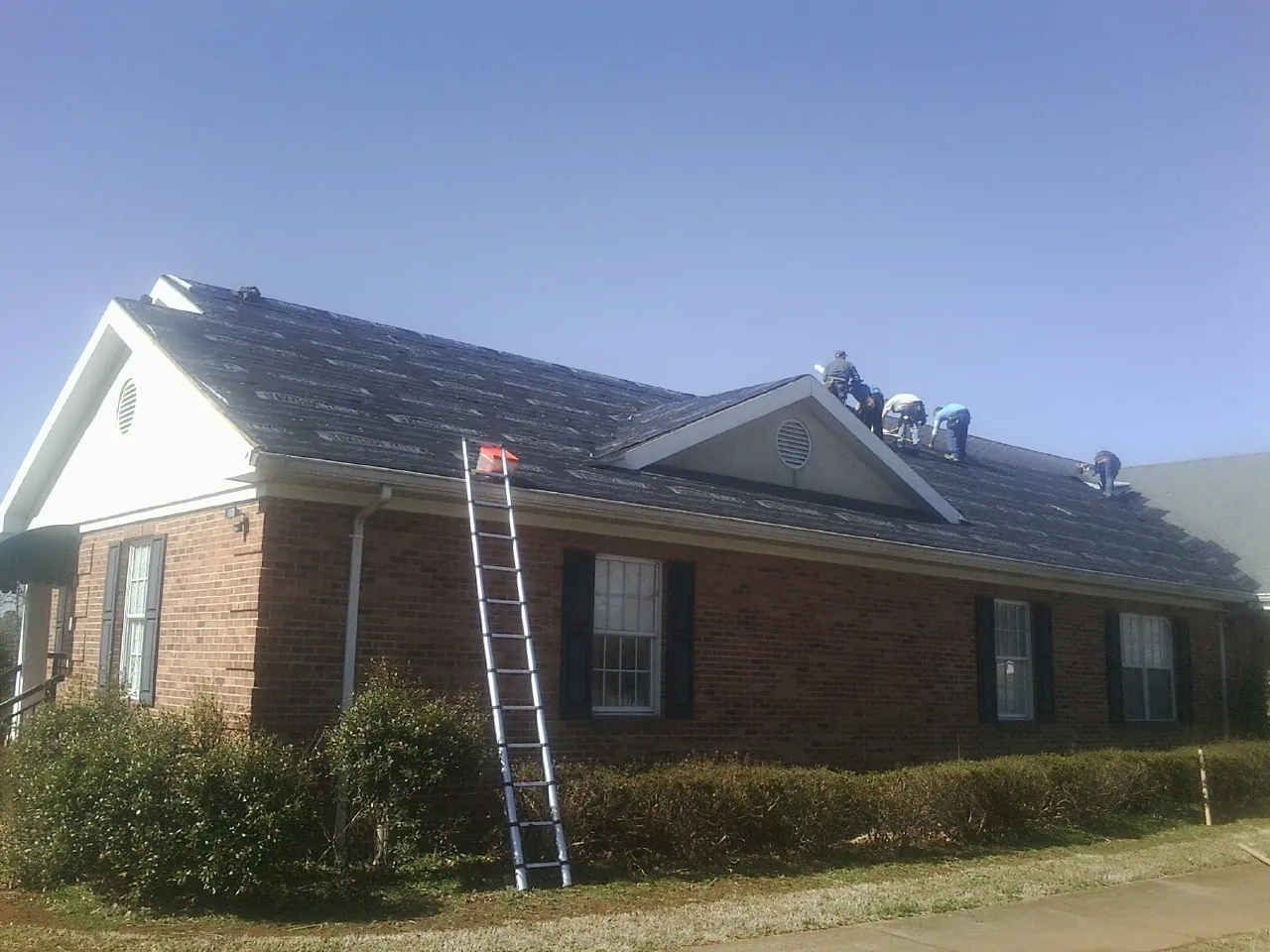 Crew tearing shingles off a brick ranch roof with a ladder set — Emergency Roof Repair work by our crew in Seffner