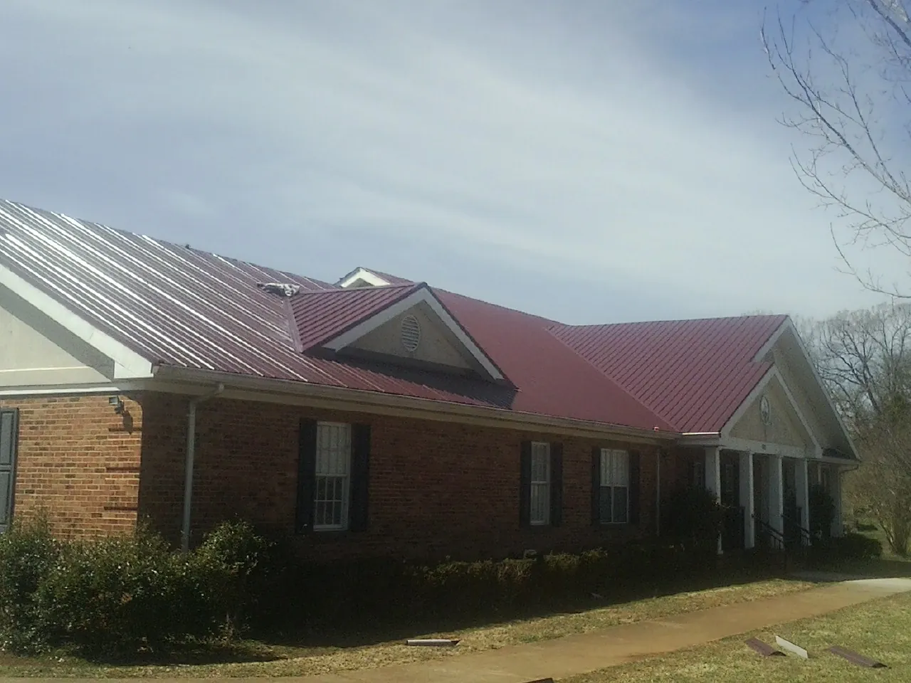 Red metal roof with gabled entries on a long brick building, from a Hail Damage Roof Repair job in Seffner