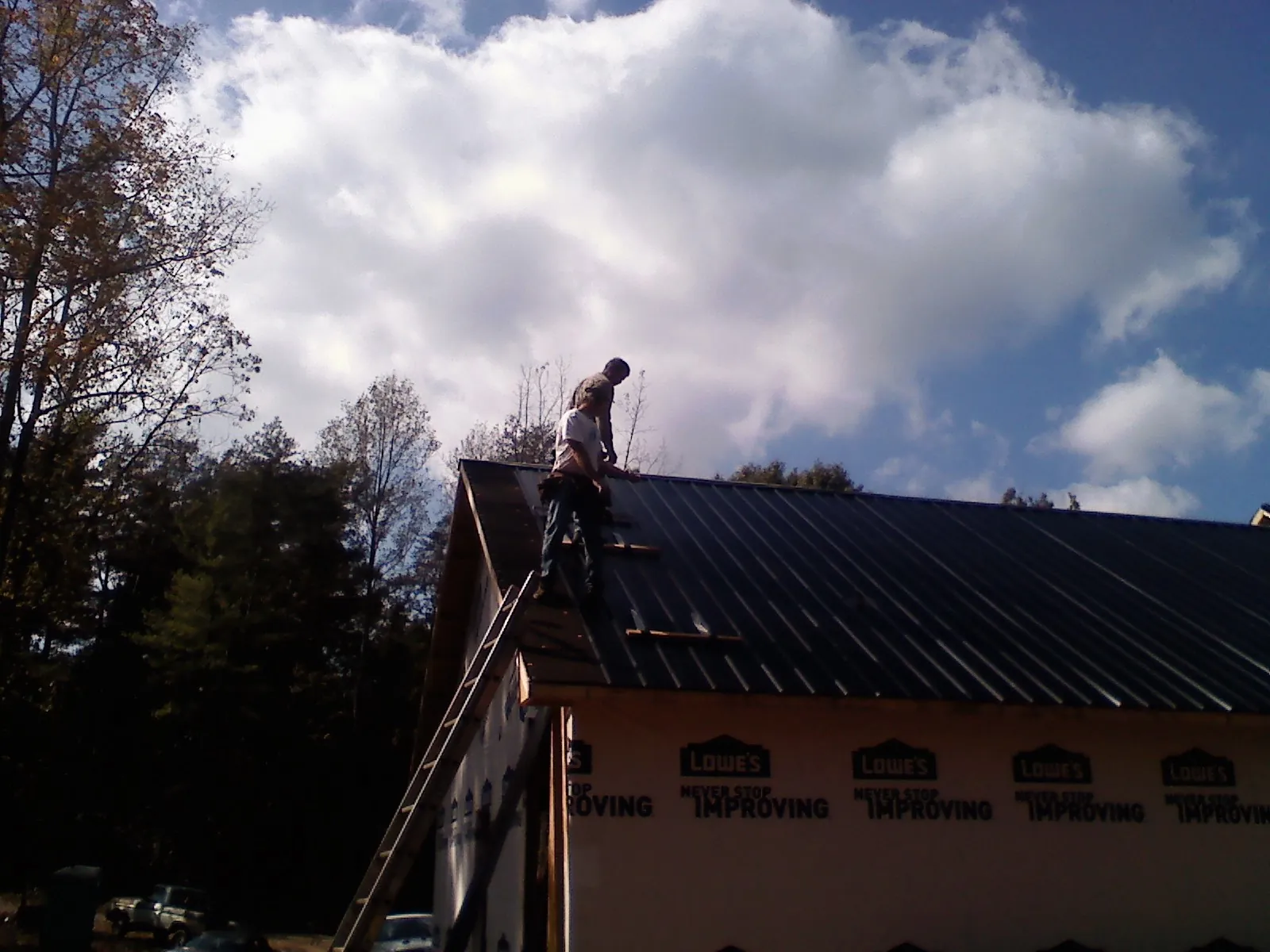Roofer fastening dark metal panels high against a cloudy sky, from a Roof Inspection job in Seffner